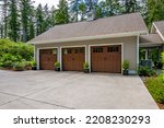 Beautiful custom built craftsman style home three car garage with wooden doors lush landscaping with spring foliage and shadows dappling the yard