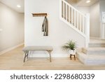 Bright and airy entry foyer with white wall stair case light colored hard wood flooring dark walnut front door entry coat rack hooks to a welcoming interior