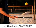 Beach tennis racket and ball. Man holding racket with sand and beach tennis ball on court.