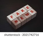 Small photo of Fake news, red words on wooden cube block on dark background. Fake, discredit, lie, confusion, incite and distortion concept.