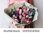 Very nice florist woman holding a beautiful colourful blossoming flowers bouquet of fresh roses, carnations, tulips, eucalyptus on the grey wall background