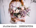 Very nice young woman holding big and beautiful bouquet of fresh roses, hydrangea, eustoma, delphinium, gypsophila, carnations in pastel cream, purple and pink colors, bouquet close up