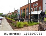 Small photo of HICKORY, NC, USA-22 JUNE 2021: Diagonal diminishing perspective view of downtown "Main Drag" showing buildings, and colorful shrubs, sidewalk, tables and chairs.