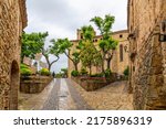 Small photo of Pals, Spain - May 25 2022: The wet tree lined streets heading to the Esglesia de Sant Pere cathedral at the medieval village of Pals, Spain after a summer rainstorm along the Costa Brava coast.