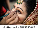 Close up of the beautiful traditional Indian bride getting ready for her wedding day. Cropped hand of makeup artist doing a makeup of bridal face and applying eyeliner.