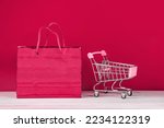 Black Friday sale concept. Mini shopping cart and bag on a red background. Color of the year 2023 - Viva Magenta