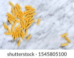 Small photo of Original Italian Penne Rigate Pasta on white marble background. Puristic Italian cuisine theme with copy space for text and design, high resolution. Pasta as a basic ingredient in the recipe.