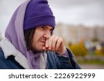 Small photo of Portrait of man sniffling in cold weather, standing on city street. Frozen guy in warm clothes with snot, wiping nose