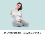 Pregnant Woman touching her belly. Pregnant middle aged mother's hands caressing her tummy. Healthy Pregnancy concept, Sitting Gravid female on blue background, full length portrait