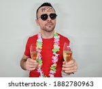 lonely attractive man posing near white wall with glass of champagne in hand. boy wearing hawaiian flowers and has PF21 written on forehead. celebrating silvester or new year 2021 at home quarantine.