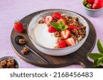 Breakfast, unsweetened yogurt with chocolate baked granola and chopped fresh strawberries in a gray bowl on a pink concrete background. Breakfast recipes. Healthy food