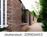Small photo of decorative wrought iron picket fence panels and stone fence piers. green garden, lush trees, plants and foliage. home ownership concept. property protection. concrete pavement. diminishing perspective