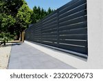 gray aluminum fence and gate. horizontal panels. narrow gaps.  powder coated finish. diminishing perspective view. modern fence design concept. concrete sidewalk. white stucco base and fence piers