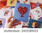 Small photo of Hand holding quilling card with red heart balloon. Happy valentine day. woman making greeting cards. Hand made of paper quilling technique. Hobby, home office. Heart from red paper ribbons