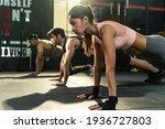 Group of athletic people men and woman with ponytail and gloves workout together. Doing plank for strenght and strong abs musclesin gym for healthy and sporty lifestyle. Sports activity training class