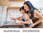 Asian loving mom teach young preschool girl to wash dishes in house. Happy family stay home in kitchen, Supportive mother spend time with little kid daughter together. Parenting Relationship concept.