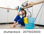 Asian young housewife feeling exhausted after doing housework at home. Attractive woman housekeeper cleaner sitting on floor, feeling tired and stress to clean mess in kitchen and overworked in house.