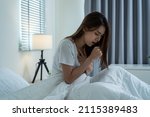 Small photo of Asian beautiful girl in pajamas feel sick while sit on bed in bedroom. Attractive sleep young woman cover her mouth, feeling bad with fever and coughing after wake up on bed in the morning at home.