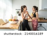 Small photo of Asian active two women sibling in sportswear eat an apple in kitchen. Young beautiful girl sister feeling happy and enjoy eating fruits healthy foods to diet and lose weight for health care in house.