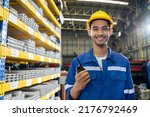 Small photo of Portrait of Asian industrial worker man working in manufacturing plant. Young handsome male industry factory engineer wear helmet while processes product at manufactory warehouse and looking at camera