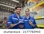 Portrait of two male industrial worker working in manufacturing plant. Young handsome male industry factory engineer wear helmet and processes order and product at manufactory warehouse with happiness