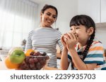 Small photo of Asian mother teach and motivate young girl child eat healthy fruit. Adorable little kid child feel happy and relax, enjoy eat apple healthy foods for health care and wellness in kitchen at home.