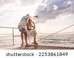 Small photo of Caucasian young couple drinking champagne while having party in yacht. Attractive man and woman hanging out, celebrating anniversary honeymoon trip while catamaran boat sailing during summer sunset.