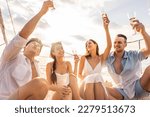 Small photo of Group of diverse friends drink champagne while having a party in yacht. Attractive young men and women hanging out, celebrating holiday vacation trip while catamaran boat sailing during summer sunset.