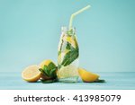Lemonade drink of soda water, lemon and mint leaves in jar on turquoise background.