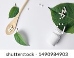 Homeopathy, naturopathy and alternative herbal medicine. Bottle with homeopathic pills on green plant leaf. Top view, flat lay with copy space over white background