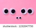 Googly eyes of family of two people with child on rose background. Close up.