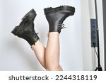 Small photo of Woman legs in black combat boots on high heel platform with lug soles upside down side view on isolated white background. Female legs wear military fashionable high heel platform combat boots