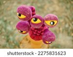 Purple striped flower with yellow eyes in clay pot on tree stump, strange crazy art object in outdoor art exhibition. Surreal big eyed flower in pot outdoor background, crazy mad weird art object