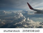 wing of airplane in sky above  clouds background of blue sky white and grey puffy clouds sky scape airplane wing in top left corner of horizontal format leaving space for type for travel vacation 