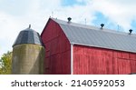 Small photo of red wooden barn with concrete silo on small hobby farm in Ontario barn with new silver metal roof freshly painted red wood slats horizontal format room for type content or logo blue sky in background