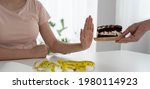 Small photo of A healthy woman pushes a plate into a chocolate cake. Abstain from eating sweets and diet concept