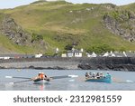 Small photo of ELLENABEICH, ISLE OF SEIL, ARGYLL, SCOTLAND, UK : 13 May 2013 : Two skiffs in the Atlantic Ocean with the white stone cottages of Ellenabeich village in the background