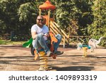 Small photo of Playful crazy man (dad) riding wooden rocking horse in a park - adult guy (hipster with beard) having fun on a playground