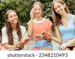 Small photo of Three teenage girls (14-15 years old) sitting outdoors, absorbed in their phones, exemplify the modern teen (generation Z) lifestyle, education, and the influence of gadgets and social media.