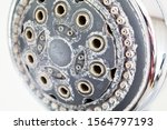 Silver round shower head with hard water deposit all around the sprinklers close up macro side shot isolated against light gray backdrop 2019