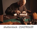 Small photo of Portrait of handsome tanner man at work, small business, authentic workshop, indoors. makes purse