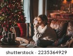 Young teen boy with long hair thoughtful look sad eyes negative mood angry and crying at home. Stylish zoomer gen Z pensive on new year holidays with xmas tree bokeh lights garlands eve 25 december