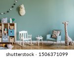 Scandinavian interior design of playroom with wooden cabinet, armchairs, a lot of plush and wooden toys. Stylish and cute childroom decor. Eucalyptus background walls. Copy space.  Template.