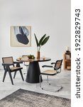 Small photo of Stylish composition of dining room interior with design table, modern chairs, decoration, tropical leaf in vase, fruits, bookcase, abstract mock up paintings and elegant accessories in home decor.