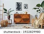 Stylish scandinavian composition of living room with design commode, black mock up poster frames, armchair, wooden stool, book, decoration, plants and personal accessories in modern home decor.