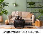 The stylish composition at living room interior with design beige sofa, black coffee table, plants and elegant personal accessories. Brown pillow and plaid. Cozy apartment. Home decor.