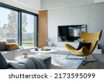 Small photo of Modern living room interior design with corner beige sofa, creative rounded coffee tables, mustard armchair and personal accessories. Panoramic windows. Template.