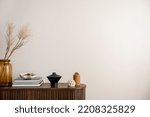 Minimalist composition of living room interior with copy space, wooden stripes commode, vase with dried flowers, candle, black books and personal accessories. Home decor. Template. 