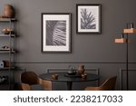 Small photo of Interior design of living room interior with mock up posters frames, round table, wooden xhair, dark wall with stucco, glass, trace and personal accessories. Home decor. Template.