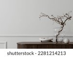 Minimalist composition of living room interior with copy space, wooden sideboard, glass vase with branch, bowl, ball sculpture and personal accessories. Home decor. Template. 